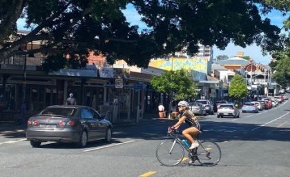 A cyclist rides across a busy road in the Brisbane suburb of West End, with a car passing in the other lane.